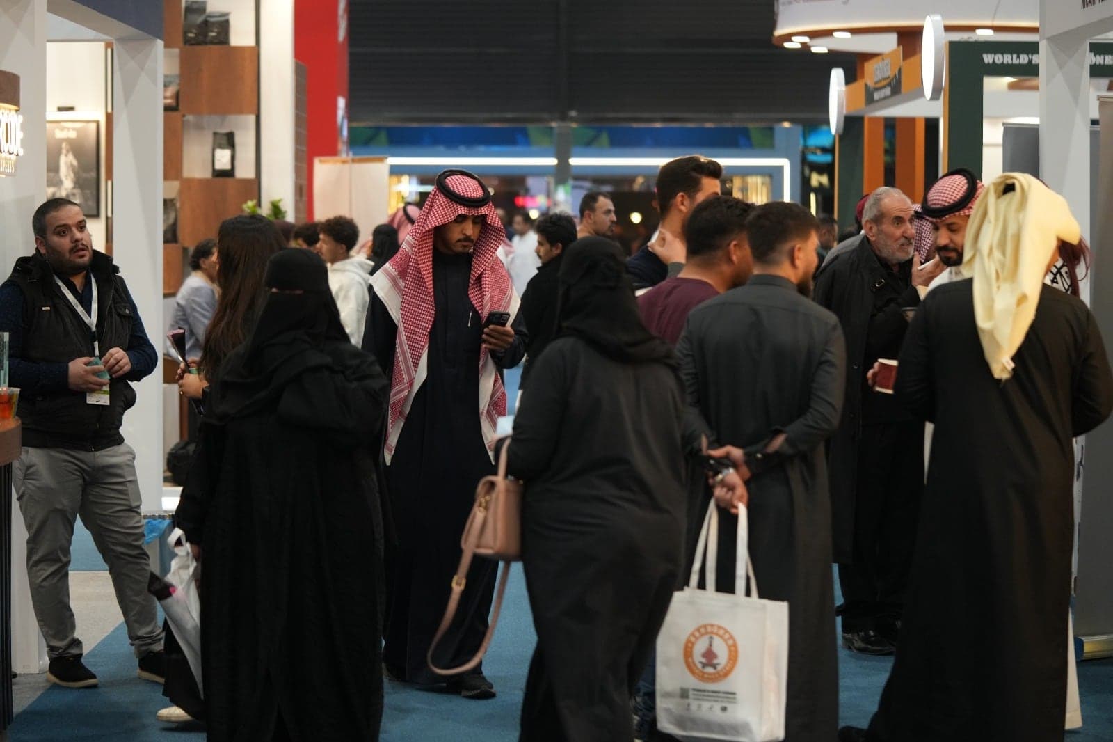 Visitors carrying brand bags as they move through the exhibition aisle